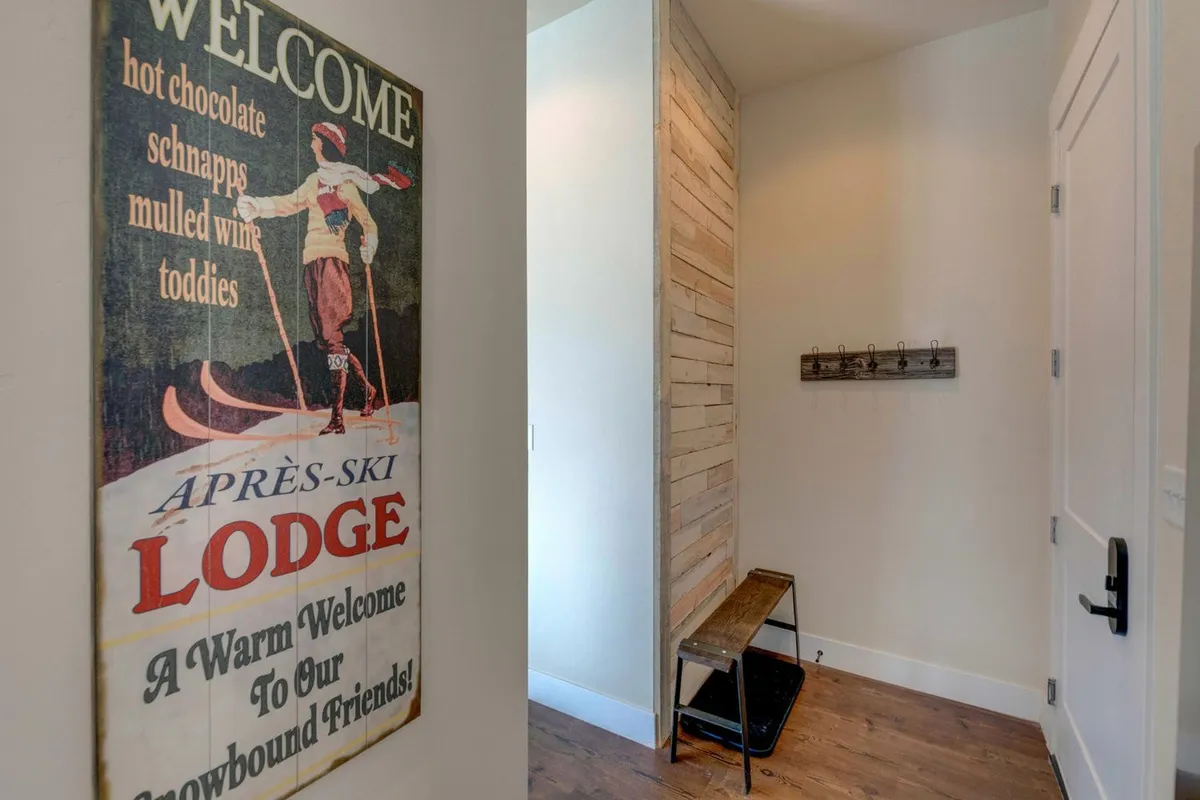 A cozy entryway or storage area featuring a vintage ski lodge sign, wooden bench, and coat hooks. Guests can hang up ski equipment and outerwear, creating a welcoming transition space after outdoor adventures.