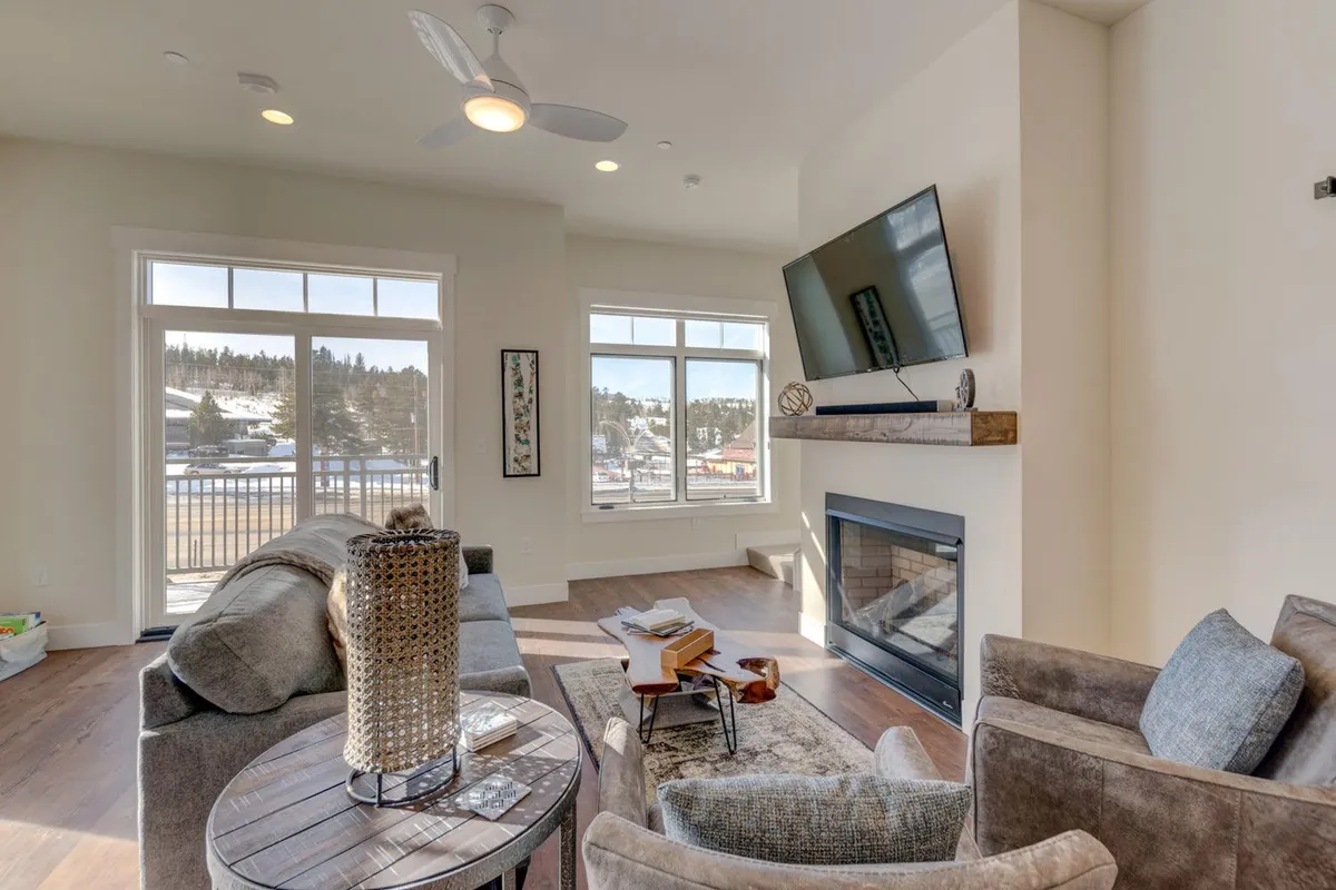 A cozy seating area with a plush sofa and coffee table facing a fireplace, set against the backdrop of large windows that frame a scenic view. The room feels inviting and perfectly suited for socializing, reading, or enjoying the mountain scenery just outside.