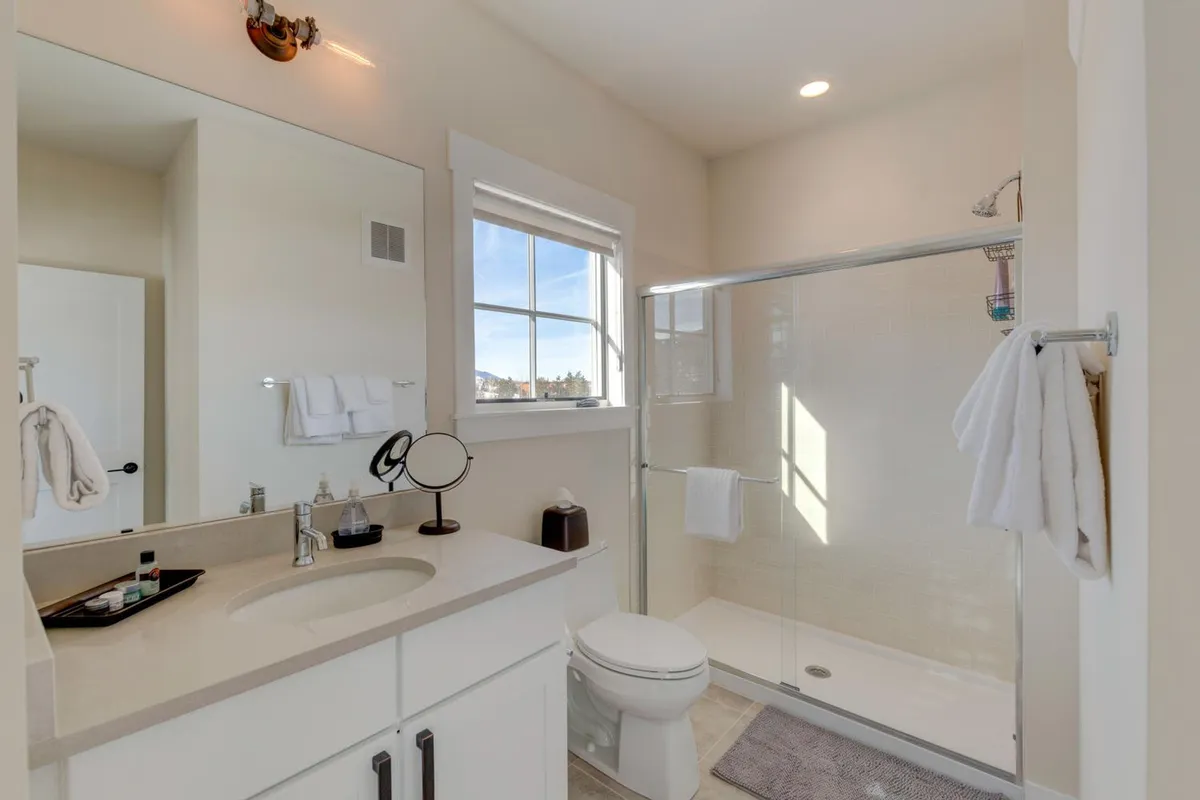 A sunlit bathroom featuring a modern vanity with a sink, a glass shower area, and a window letting in natural light. The space feels fresh, inviting, and spa-like.