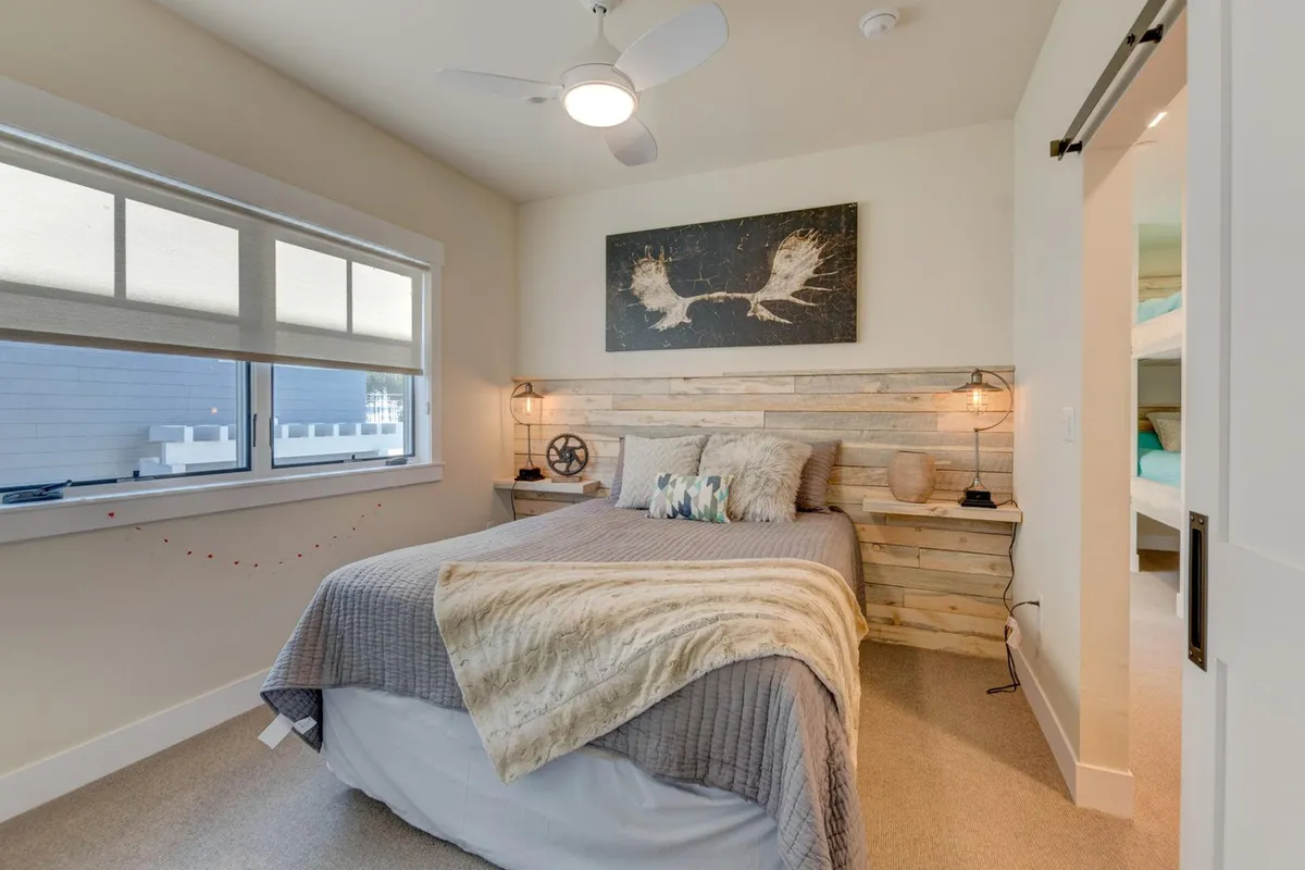 This image showcases a serene bedroom featuring a bed with textured bedding, a wooden accent wall, and an art piece above the bed. Soft natural light brightens the space, creating a calm and restful ambiance.