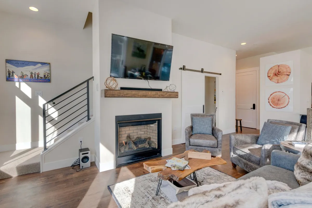 A cozy living room with a prominent fireplace, a sleek HD smart TV, a stylish wooden coffee table, and ample seating arranged for relaxation and entertainment. Morning light floods the space, enhancing the welcoming mood and highlighting the room’s modern finishes.
