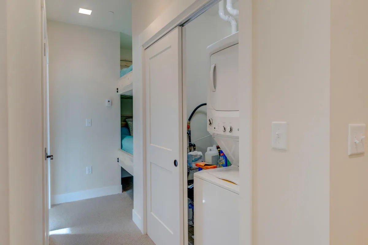 A practical, inviting laundry area shows a washer and dryer adjacent to a bunk bed setup, suggesting family-friendly accommodations. The setting is functional yet cozy, with light-colored walls and natural light, highlighting convenience and comfort.