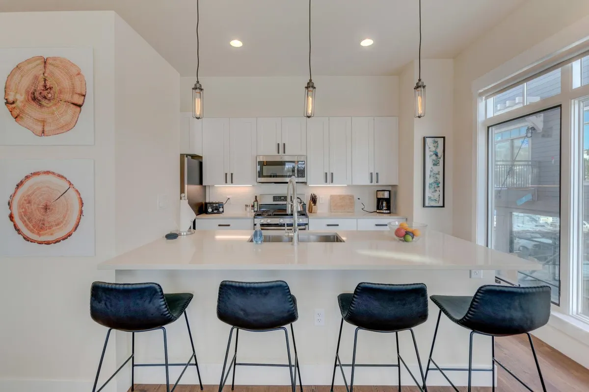 A stylish kitchen featuring a central island with bar stools, gleaming modern appliances, and contemporary wall art. The layout invites socializing while cooking, and the setup is ideal for casual dining or entertaining friends and family.