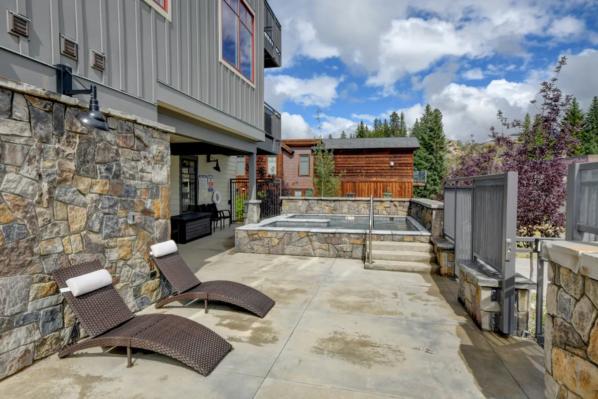 An inviting exterior shot of a stone patio with lounge chairs and an oversized hot tub surrounded by greenery, perfect for post-adventure relaxation and socializing. The tranquil setting highlights the property’s resort-style amenities.
